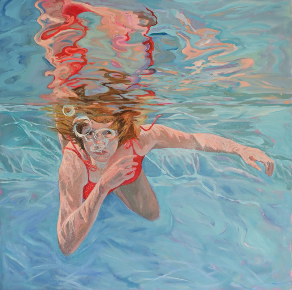 woman in red bathing suit swimming underwater with colored reflections on the surface of the water.