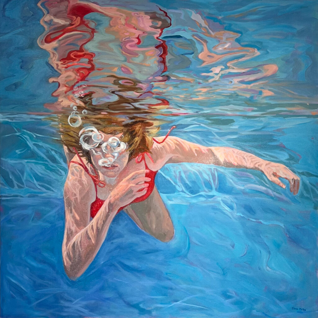 A woman in a red bathing suit swimming underwater toward the viewer and blowing bubbles