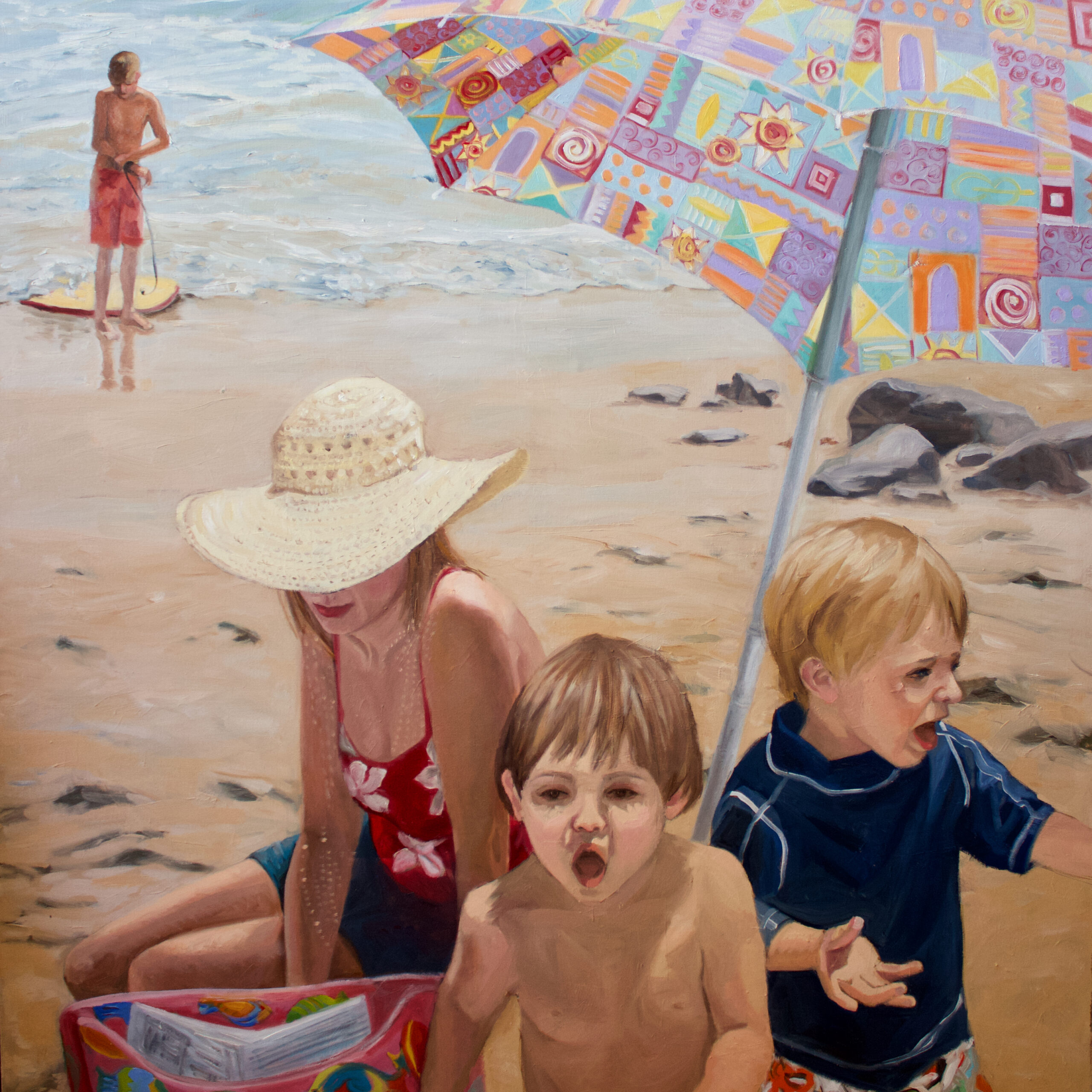 A mom and two little boys playing on the beach under a sun umbrells with the ocean in the background